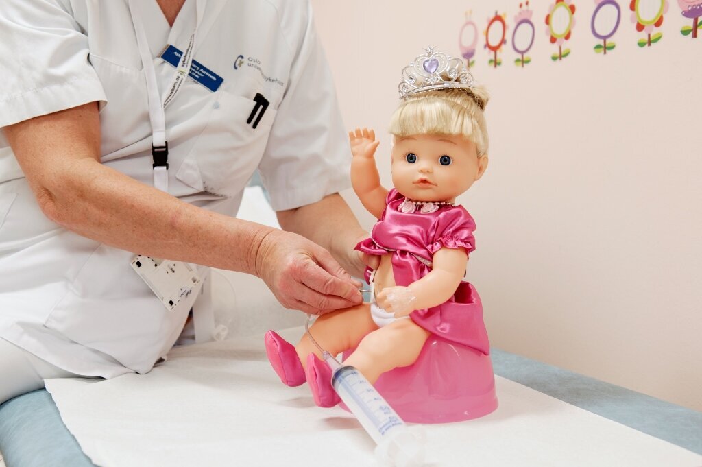 Bildet viser en dukke som sitter på rosa potte og har åpning på magen som brukes til å skylle tarmen.