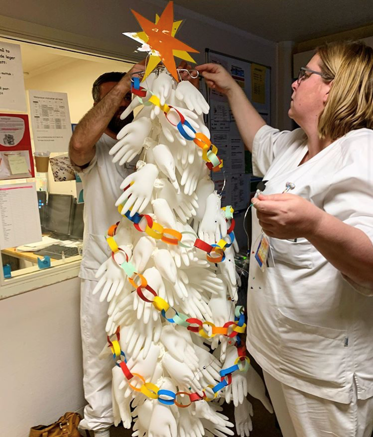 Bildet viser to sykepleiere som pynter et juletre laget av hansker.