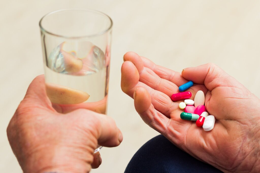 Bildet viser to hender, den ene holder i et glass vann, den andre en håndfull tabletter.