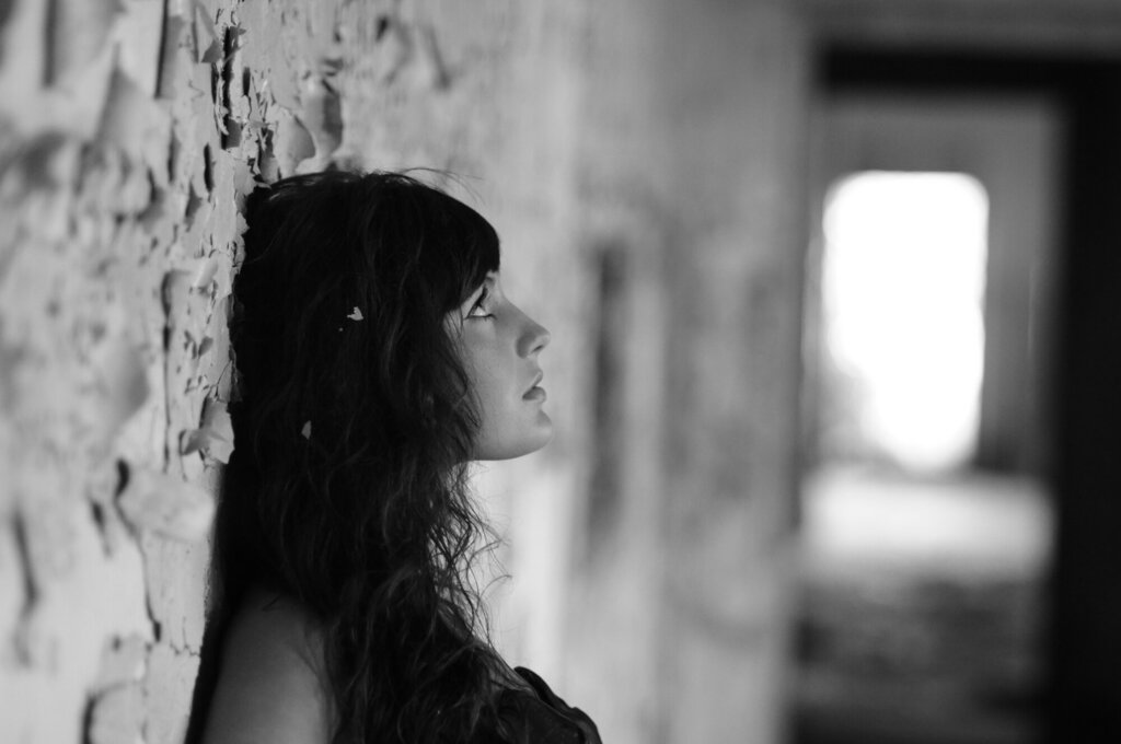 Bildet viser en ung kvinne som står lent inntil en mur og ser tankefull ut.