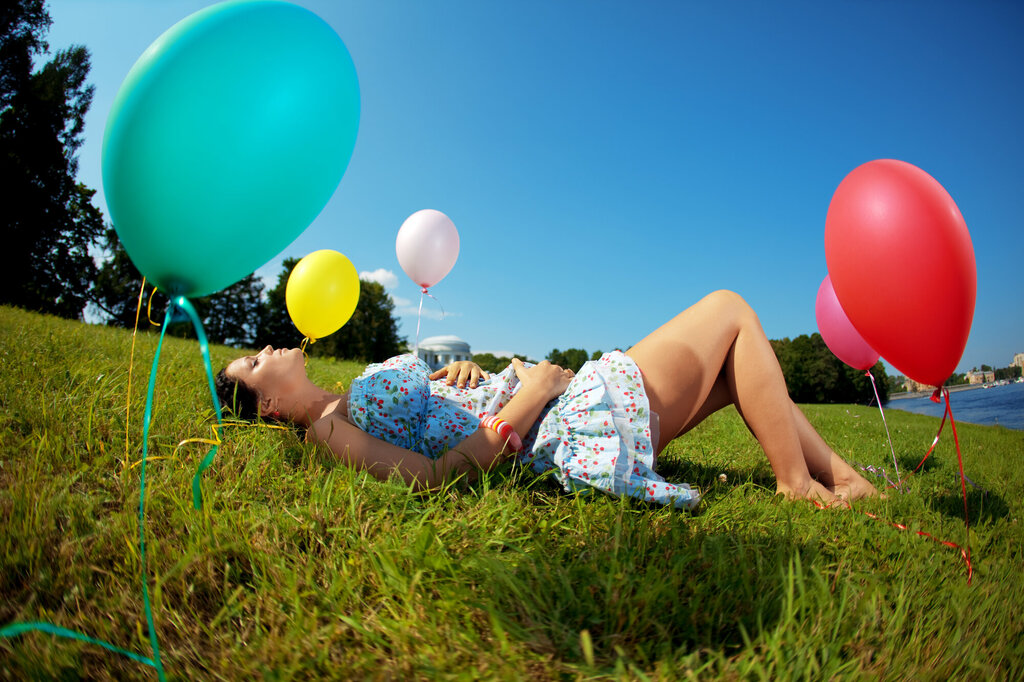 Bildet viser en gravid kvinne liggende i en eng med ballonger rundt omkring.