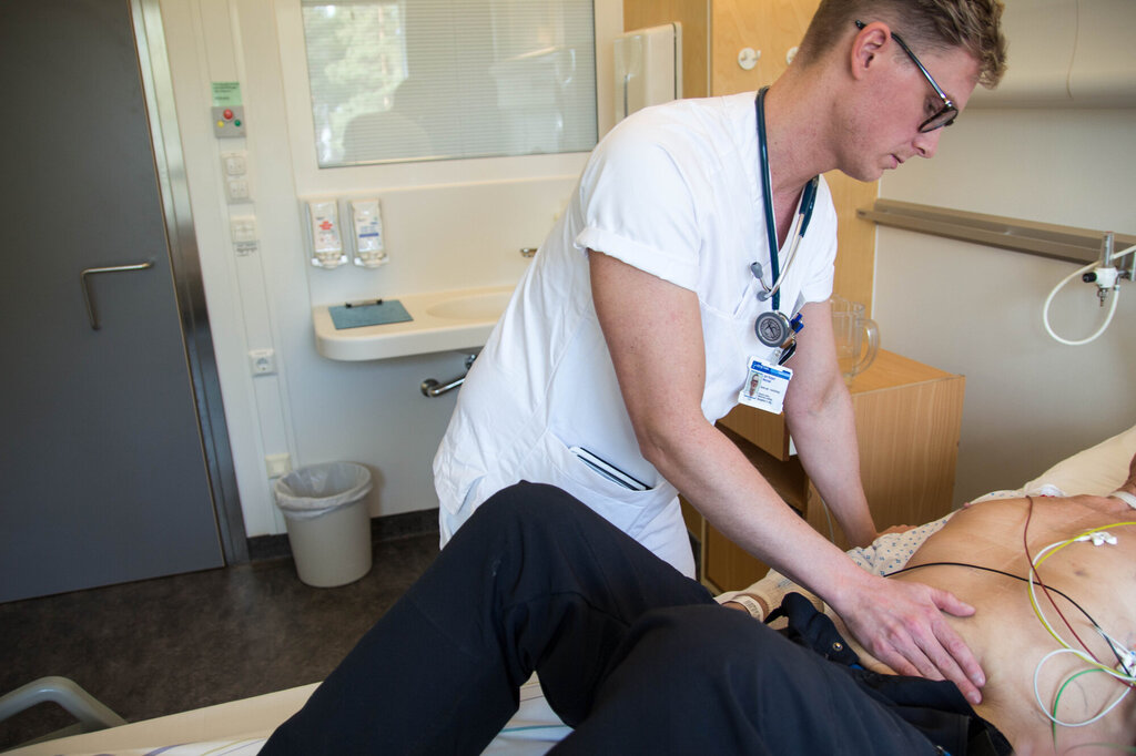 Bildet viser Jarl Robert Wexhall som palperer magen til en pasient.