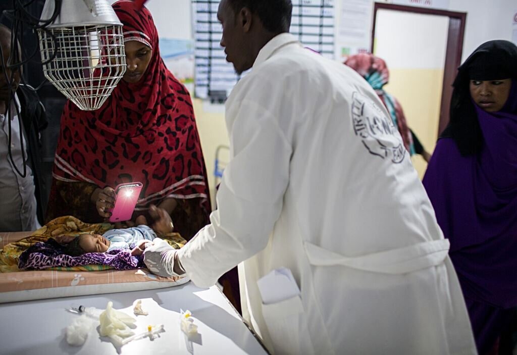 Sykepleier Faduma Hassan lyser med lommelykta på mobilen når en av legene sliter med å finne blodåren på en nyfødt. 