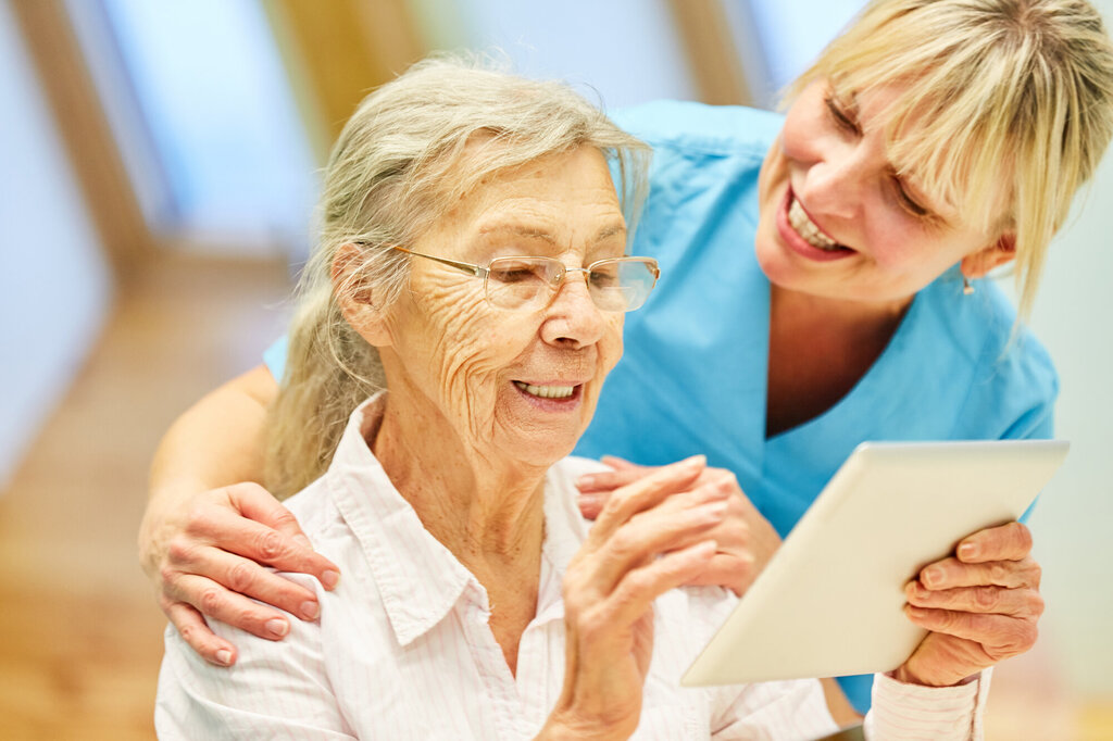 Bildet viser en eldre kvinner som ser på en iPad sammen med en sykepleier