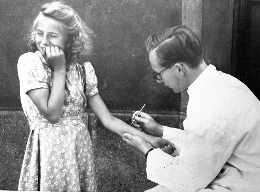 Bildet viser en jente som ser bort, med et lite angsfylt smil rundt munnen, mens en lege tar tuberkulintest.