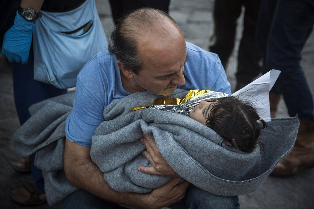 Bildet viser en mann med et lite barn inntullet i teppe i armene.