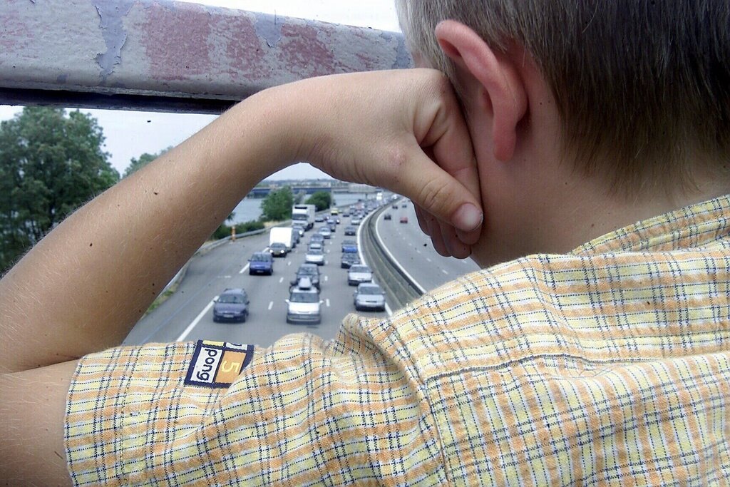 Ung gutt som står og skuer ut over motorveien fra bru