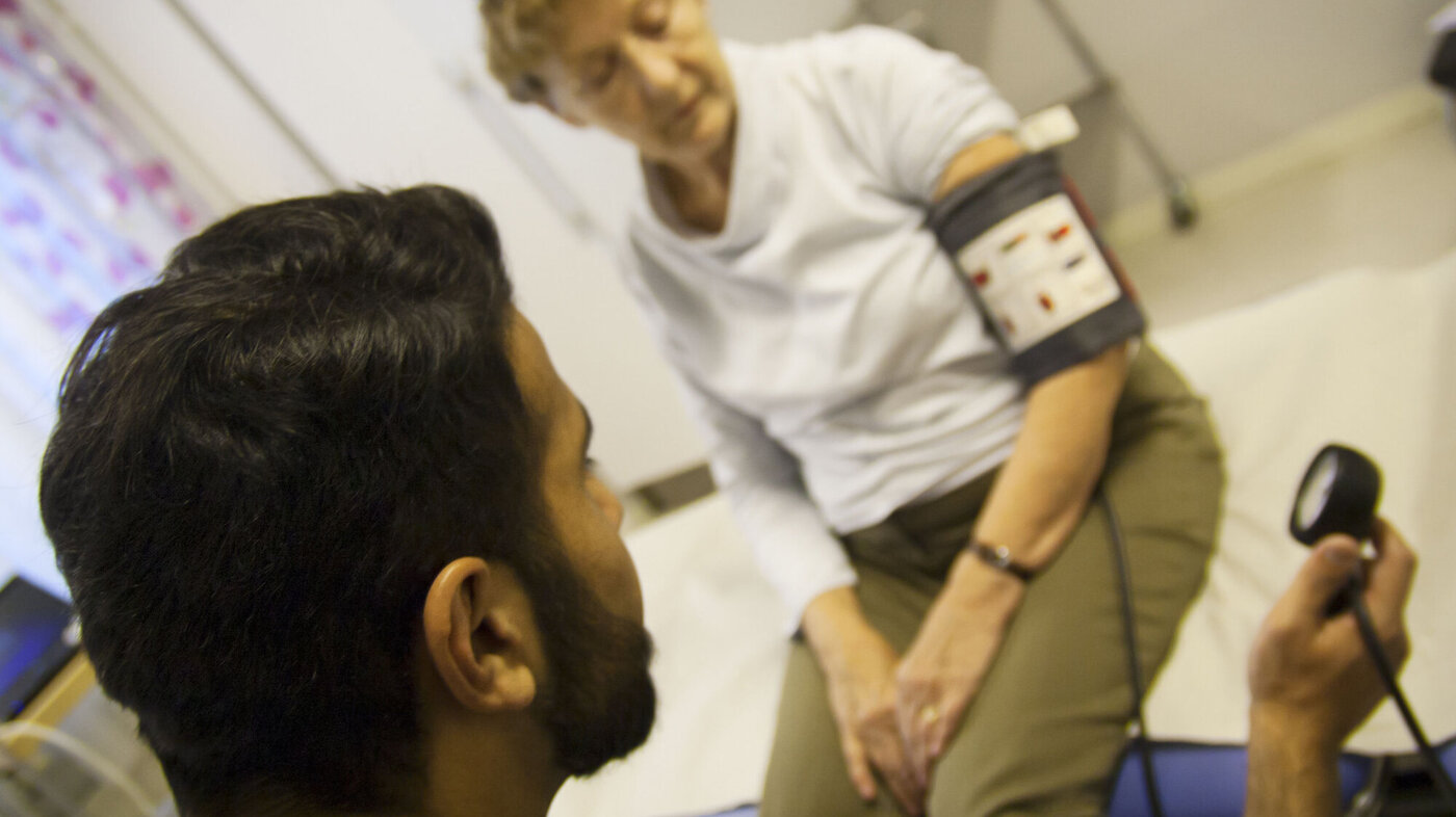 Mannlig sykepleier måler blodtrykket til eldre kvinne.