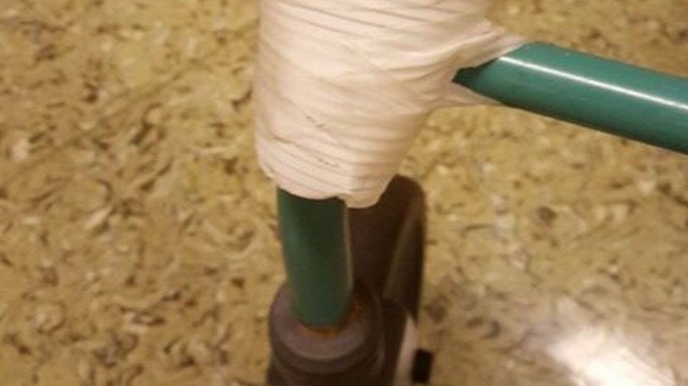 Bildet viser en plastkopp teipet fast foran nede på en rullator.