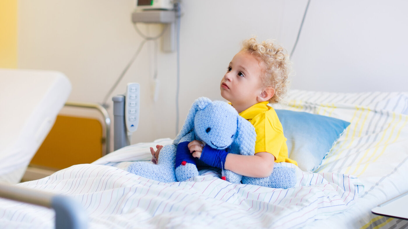 Bildet viser et lite barn som sitter i en sykehusseng.