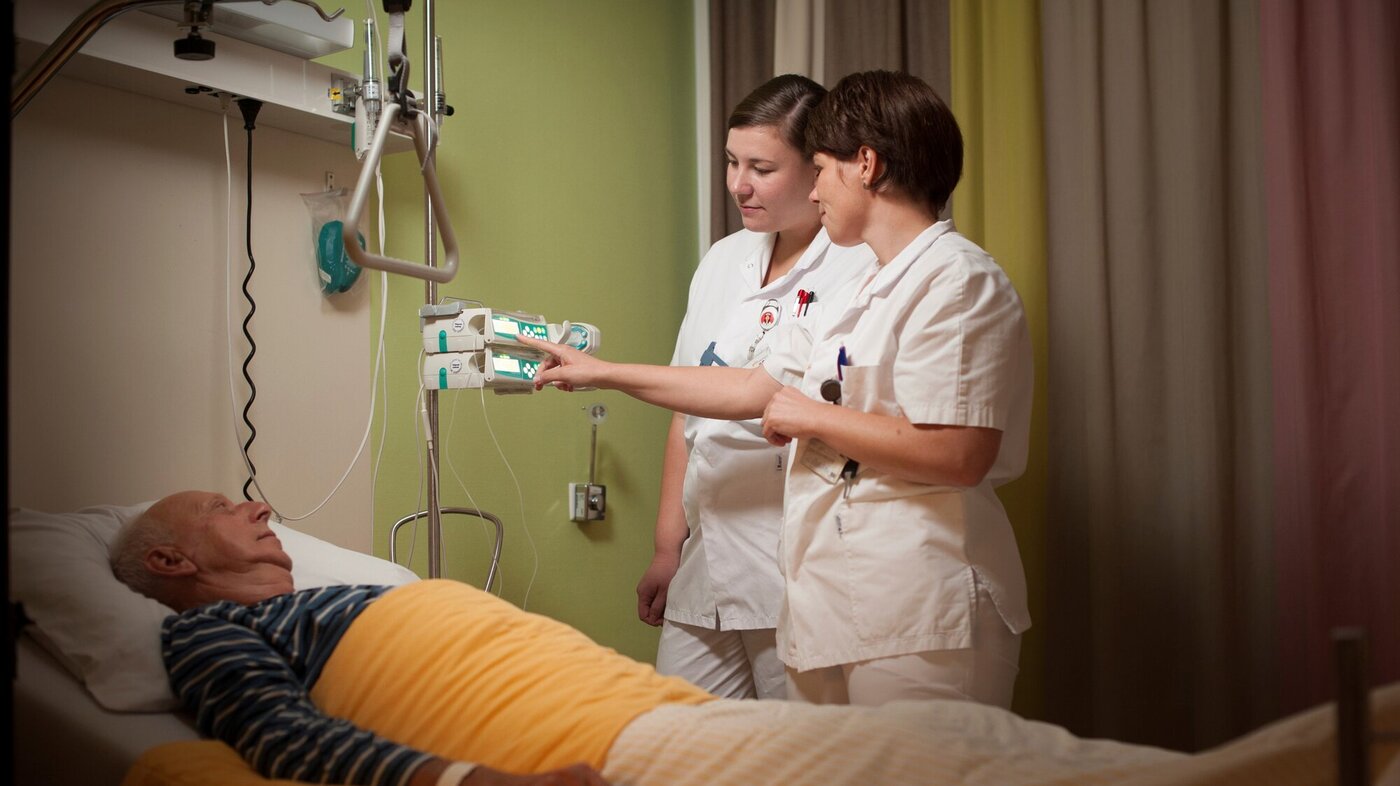Bildet viser en veileder og sykepleierstudent ved en pasient i senga