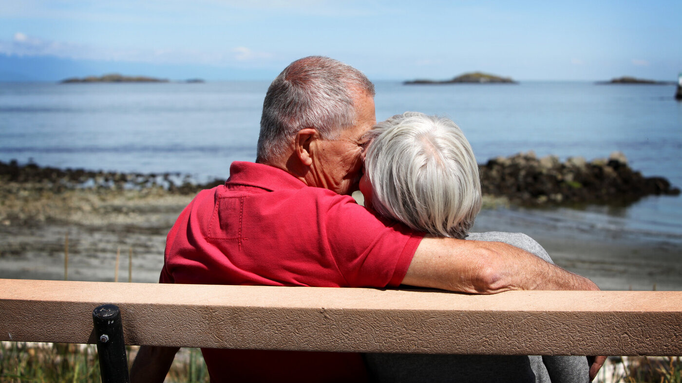 To eldre mennesker som sitter og kysser på en benk