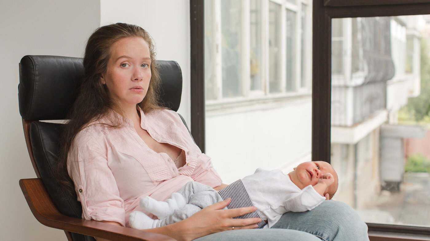 Bildet viser en nedstemt mor som sitter med babyen liggende på fanget