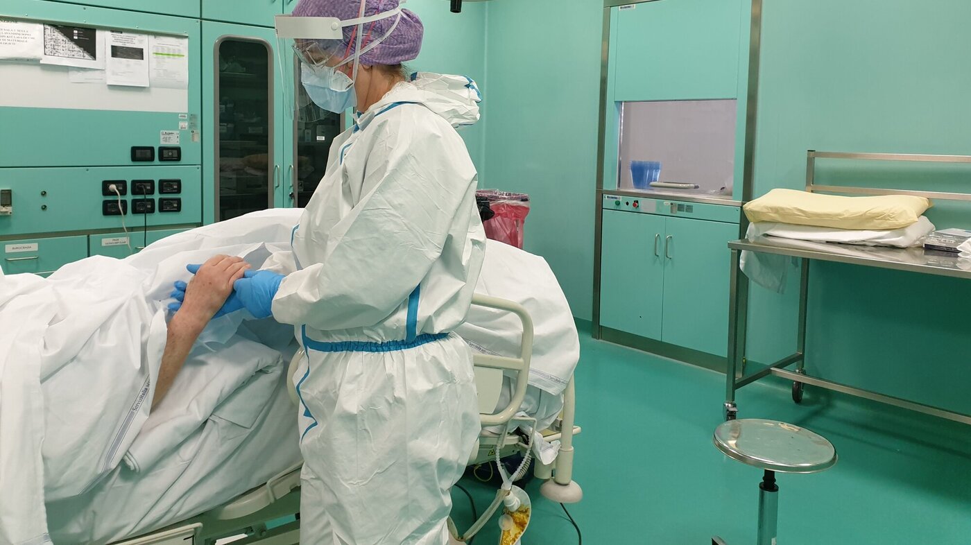 Bildet viser en sykepleier i smitteverndrakt som holder en pasient i hånden.