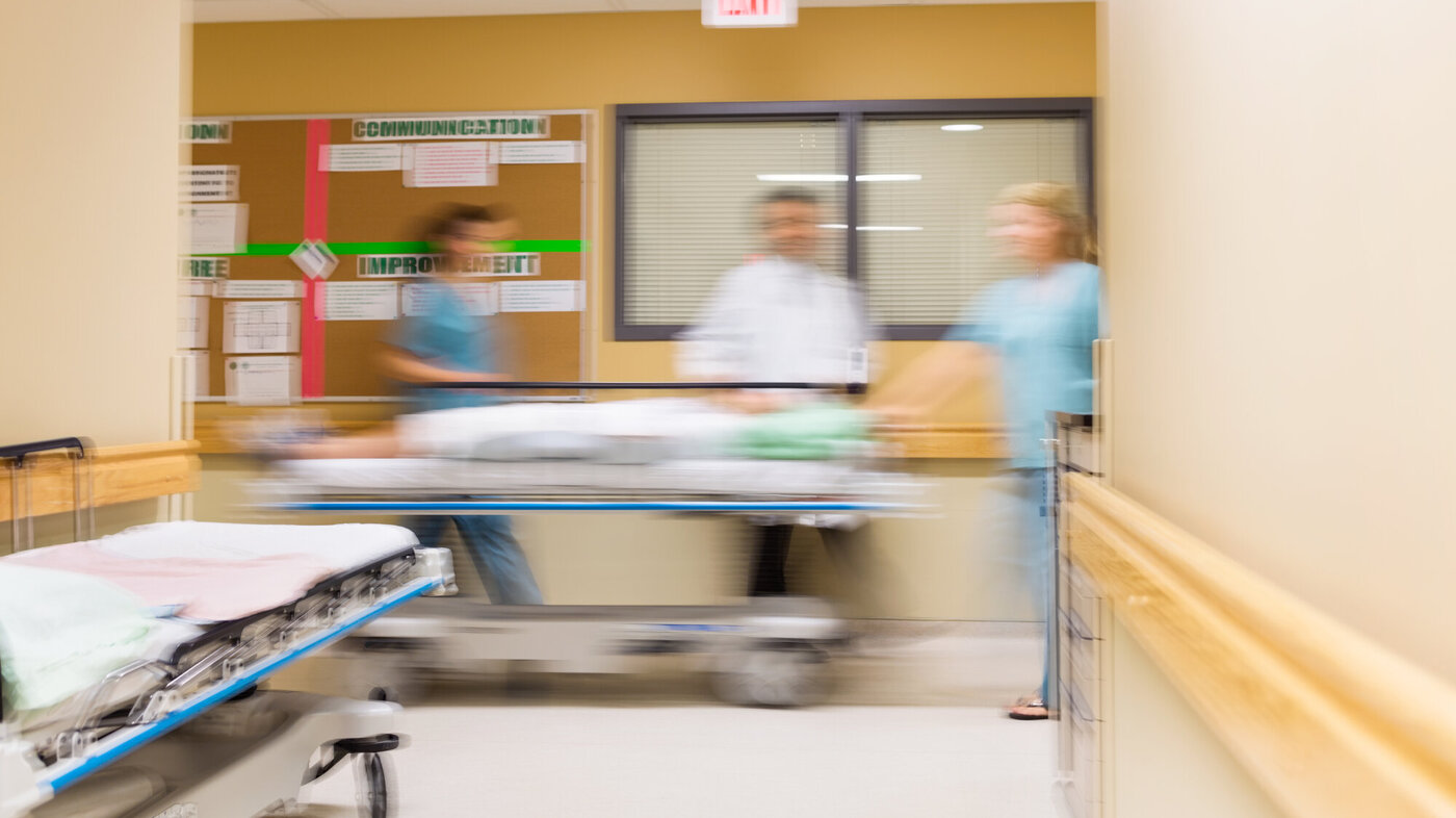 Bildet viser helsepersonell som triller en pasient i korridoren på et sykehus