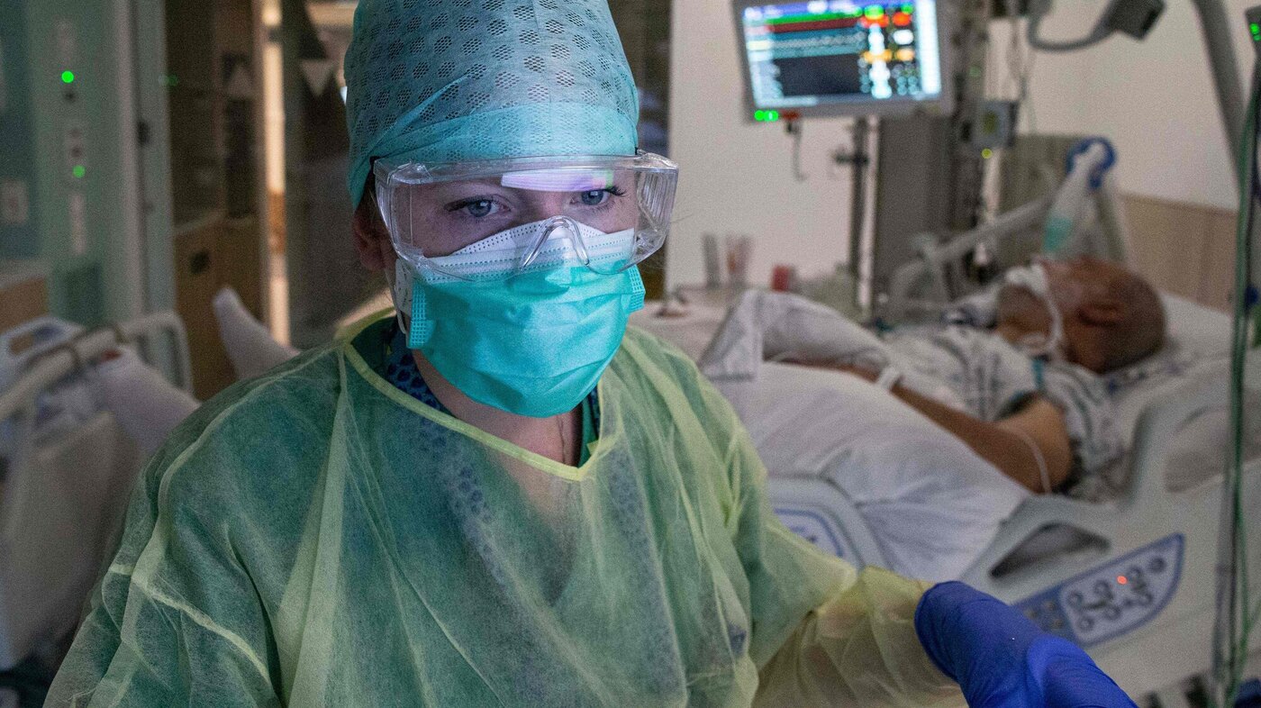 Bildet viser en sykepleier i smittevernutstyr og en pasient som blir overvåket i bakgrunnen.