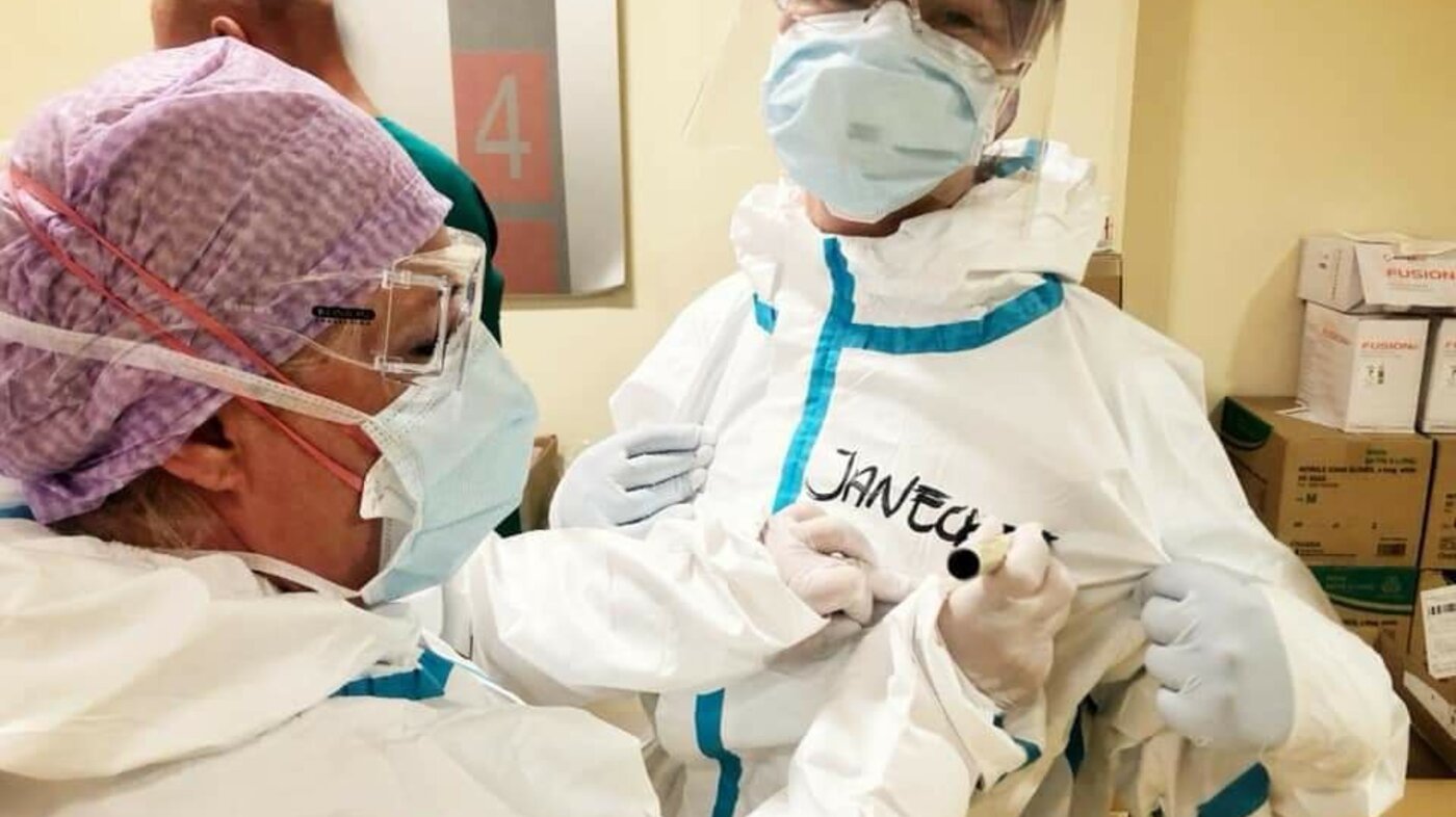 Bildet viser en sykepleier i smittevernutstyr som skriver navn på dressen til en annen sykepleier.