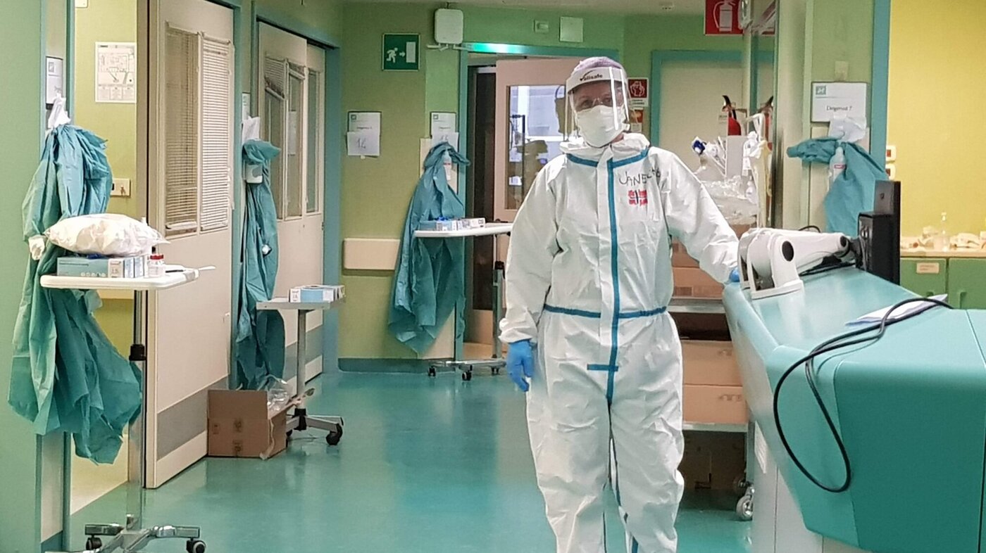Bildet viser en sykepleier i smittevernutstyr i en sykehuskorridor.