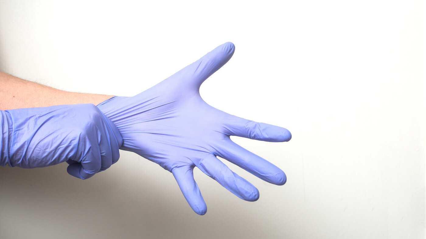 Bildet viser to hender som tar på blå hansker.