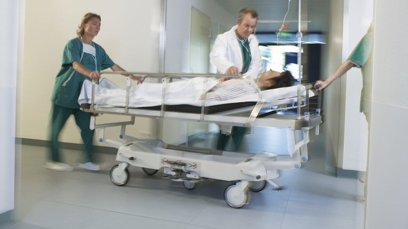 Bildet viser en pasient i en sykehusseng som blir trillet av helsepersonell