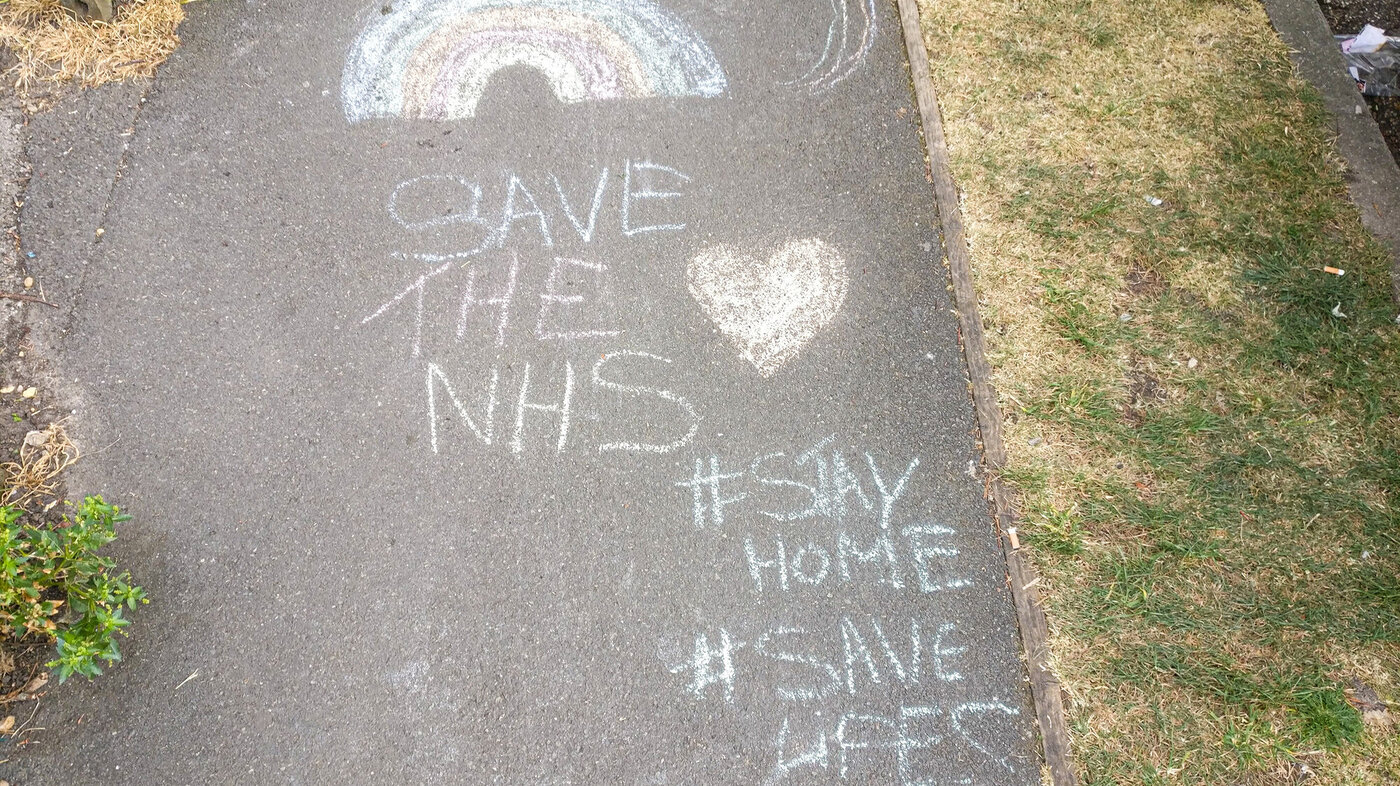 Bildet viser en krittegning på asfalten hvor det blant annet står Save the NHS