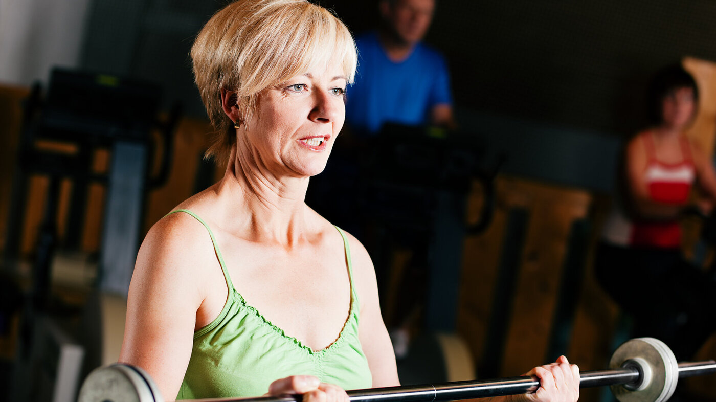 Bildet viser en eldre kvinne som trener med en vektstang