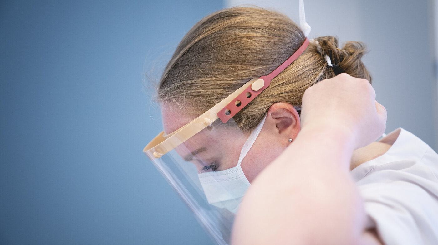 Helsearbeider, visir, smittevern Bildet viser en helsearbeider som tar på visir.