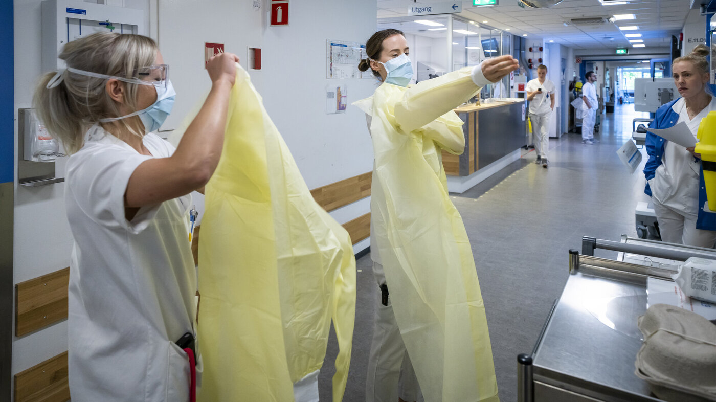 Bildet viser to sykepleiere som tar på gule smittevernfrakker.
