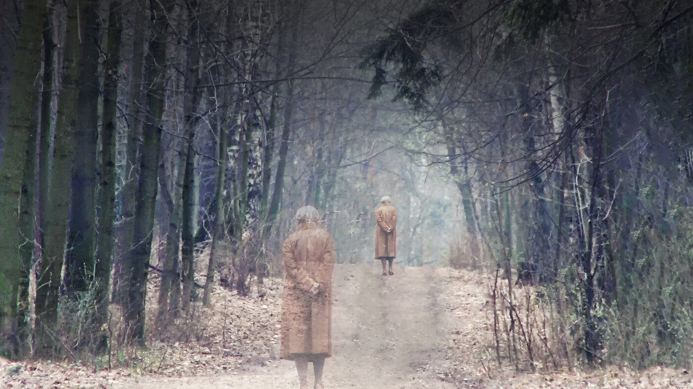 Bildet viser en eldre kvinne som går alene på en sti i skogen.