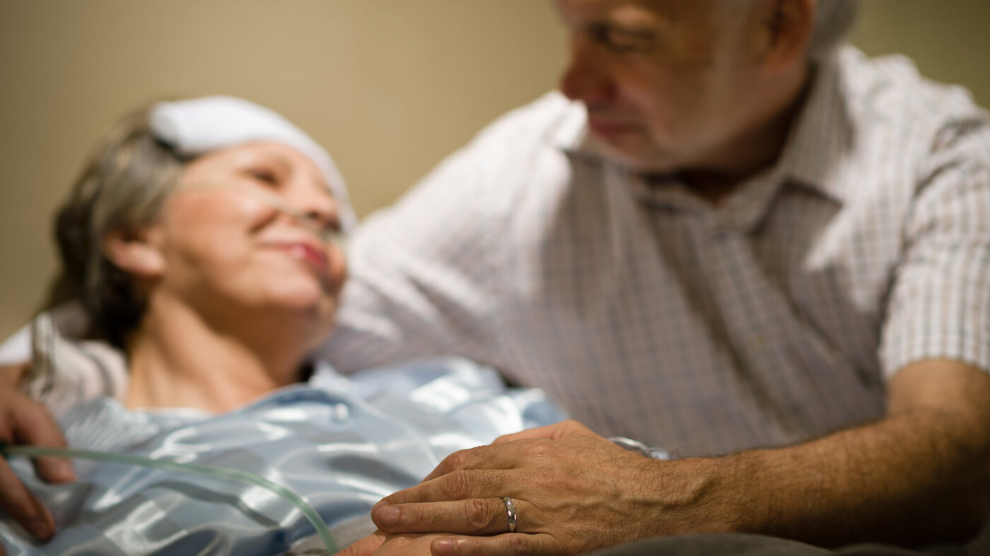 Bildet viser eldre mann ved sykeseng til kona