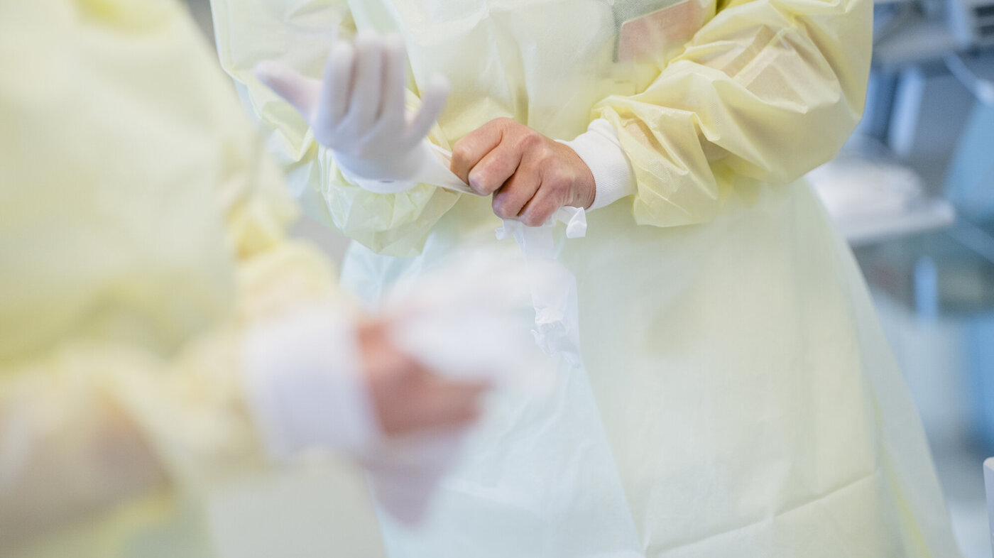 Bildet viser sykepleiere i gult smittevernutstyr som tar på seg hansker.