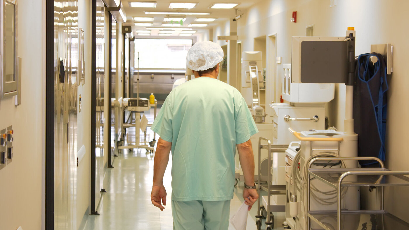 Bildet viser ryggen på en helsearbeider som går nedover en korridor på sykehus.