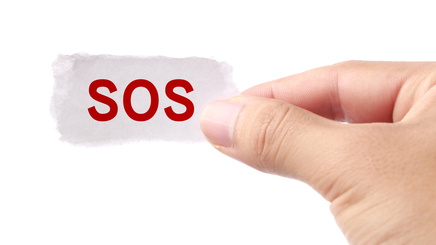 Bildet viser en hånd som holder en liten lapp påskrevet SOS