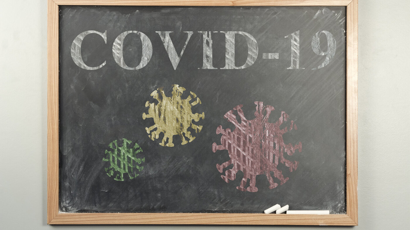 Bildet viser en skoletavle. På tavlen står det skrevet covid-19 og det er tegninger av koronaviruset.