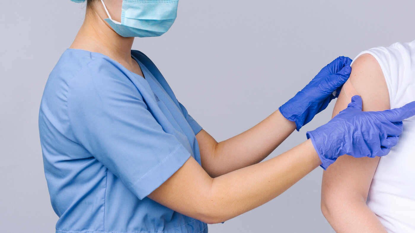 bildet viser en lege som plastrer en arm som har fått et sprøytestikk