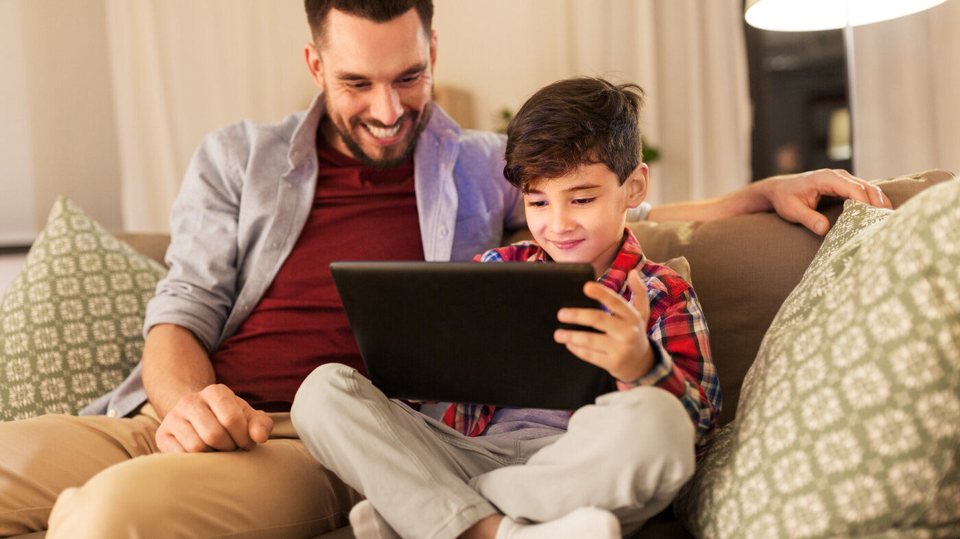 Bildet viser et barn som ser på et nettbrett sammen med sin far