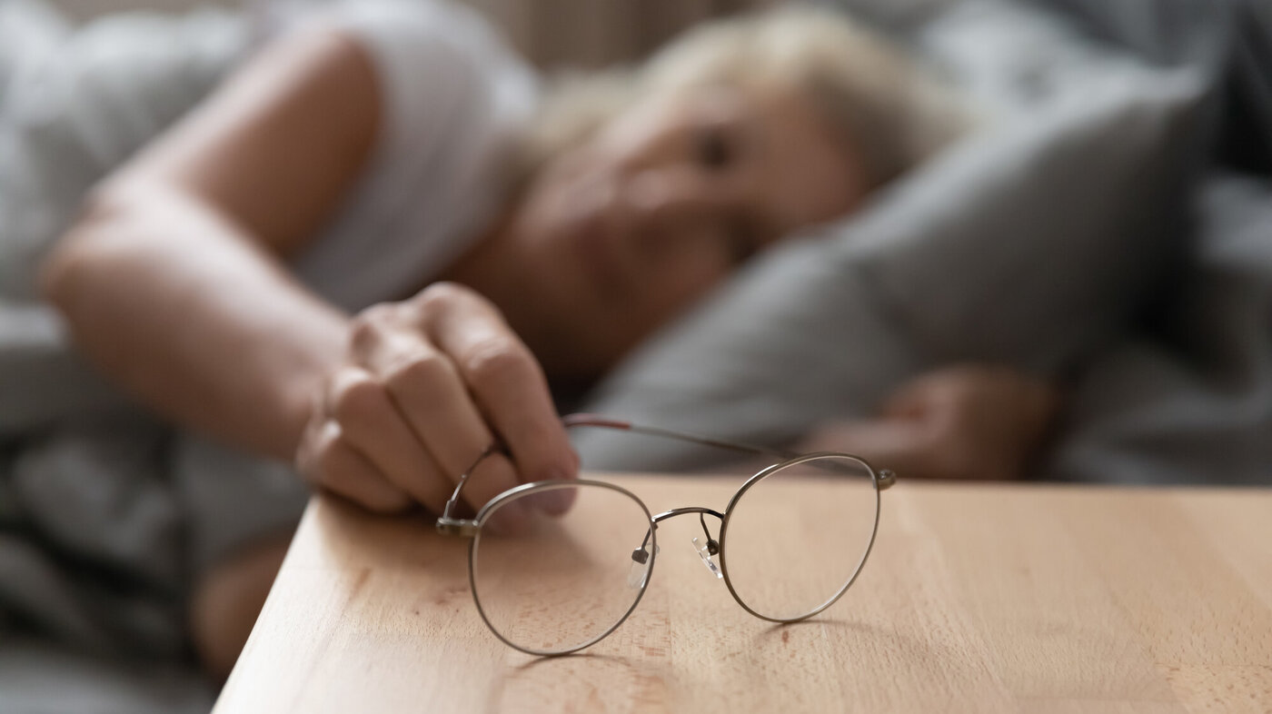 Eldre kvinne legger briller på nattbordet