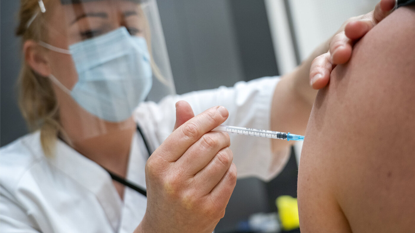 Vaksinesprøyte settes i arm av helsepersonell.