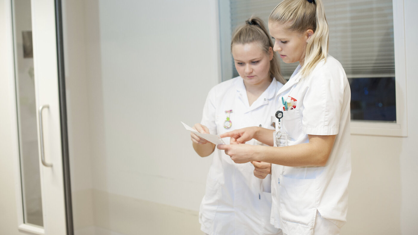 Bildet viser to sykepleiere som står og ser på et ark.