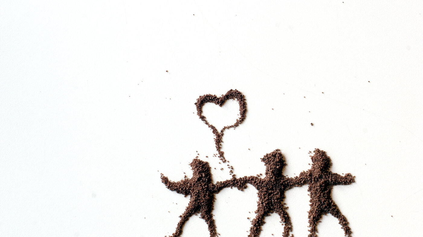 Bildet viser tre dansende figurer tegnet opp i sand med en prateboble mellom seg formet som et hjerte