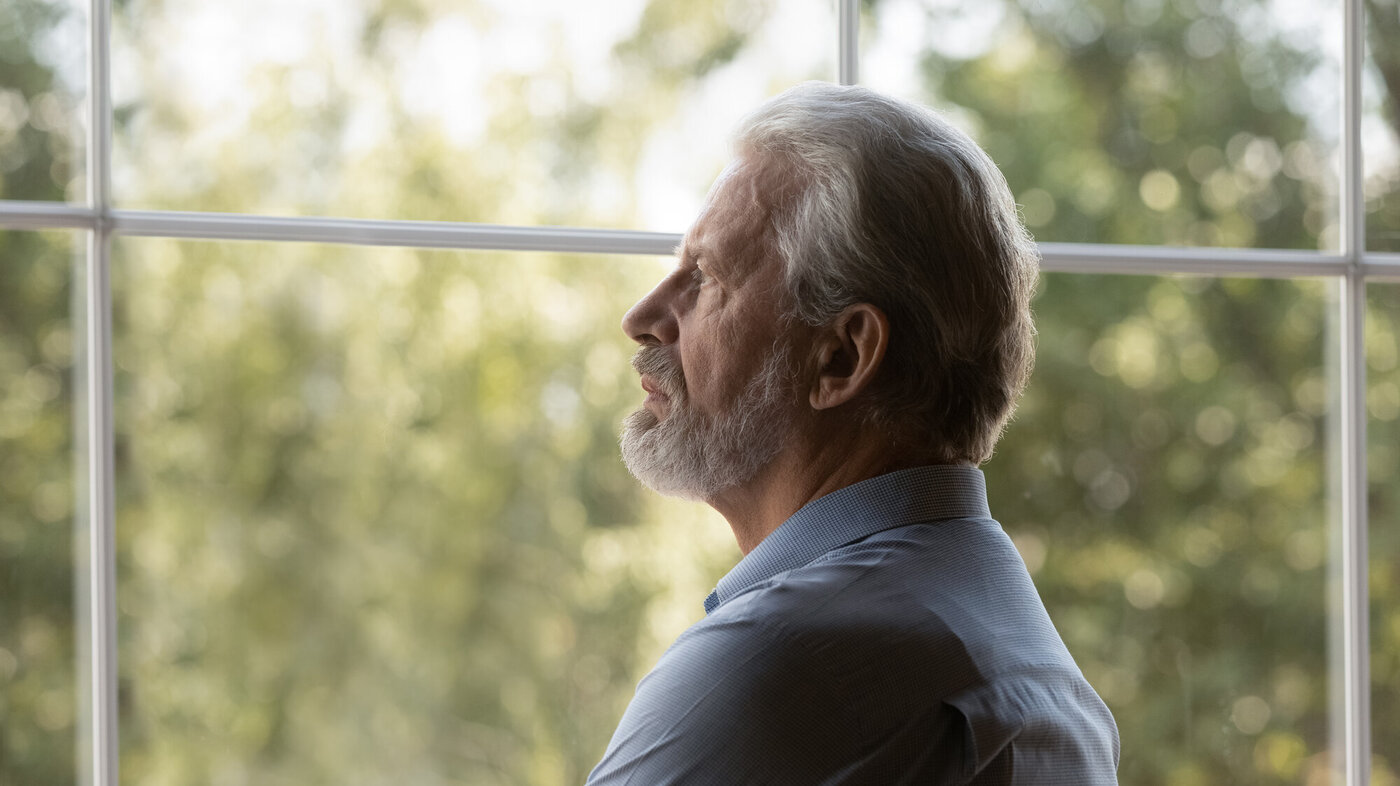 Bildet viser en eldre mann som titter ut av vinduet. Han ser tankefull og bekymret ut