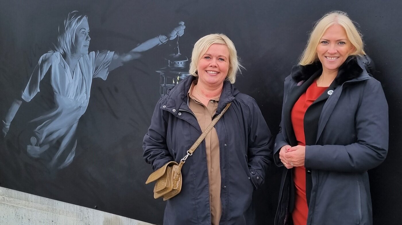 Bildet viser sykepleier Birgitte Øverdal og Lill Sverresdatter Larsen som poserer foran kunstverket etter avdukingen i Bodø.