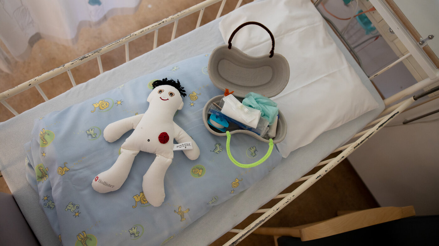 Bildet viser en dukke og et førstehjelpsskrin laget av et pussbekken, som ligger i en sykehusseng.