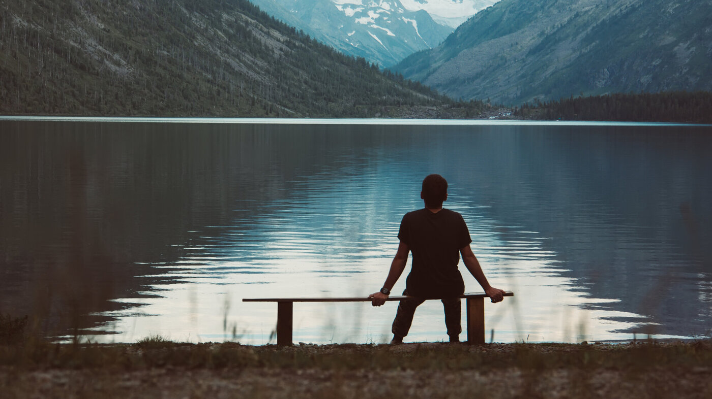 Bildet viser en mann som sitter alene på en benk og ser utover fjorden