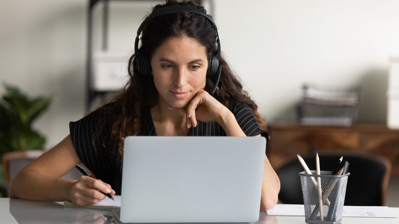 En ung kvinne med hodetelefoner ser på PC-en