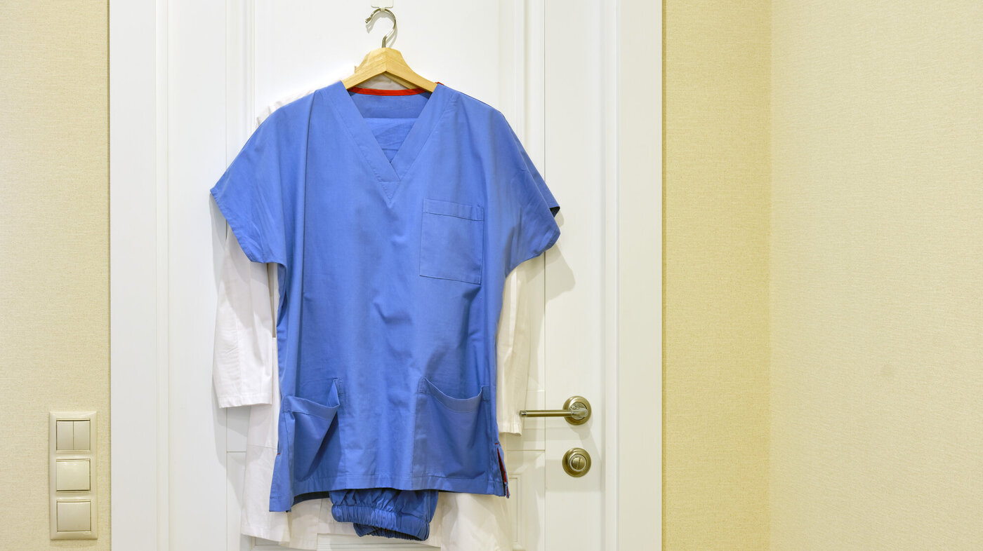 Bildet viser en sykepleieruniform som henger på en dør.