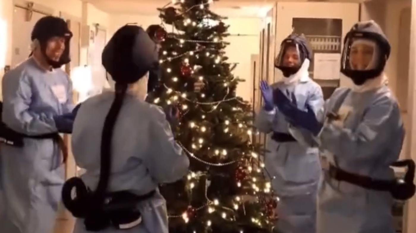 Bildet viser sykepleiere i smittevernutstyr som går rundt juletreet