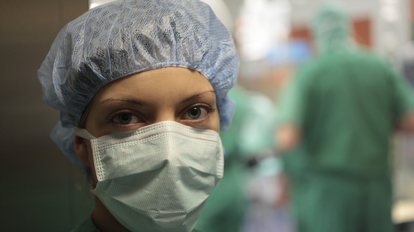 Bildet viser en sykepleier med munnbind foran en operasjonssal