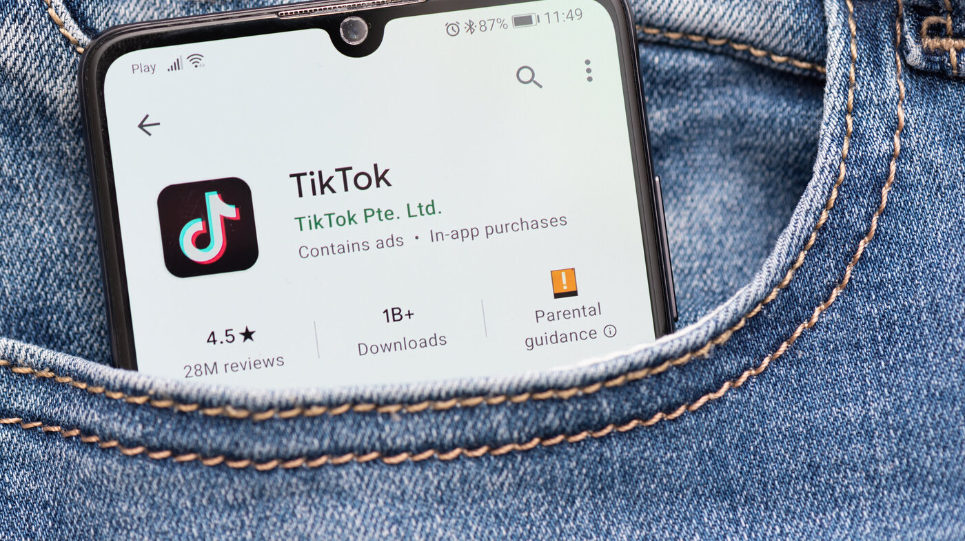 Bildet viser en mobil med TikTok som stikker opp av en bukselomme.