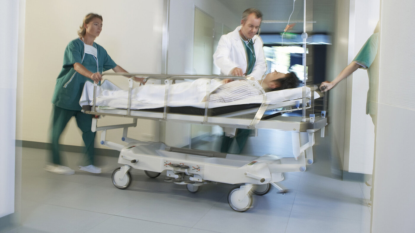 Bildet viser en sykepleier og en lege som triller en seng med en pasient.